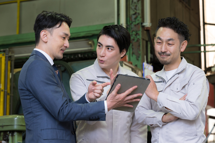 ipadを持ったスーツの男性と作業服の男性が話し合っている画像